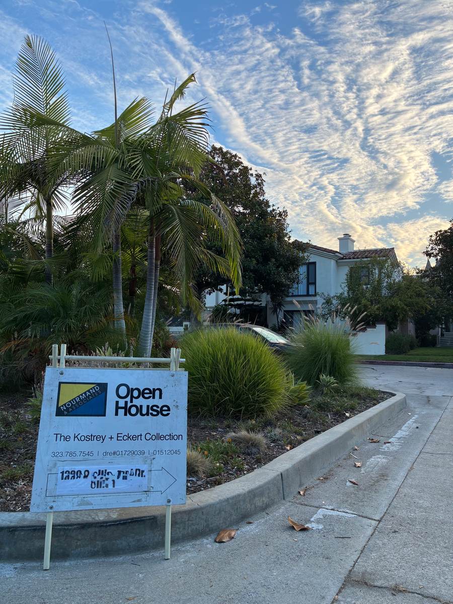 Open house sign placed near palm trees in front of a Spanish-style home