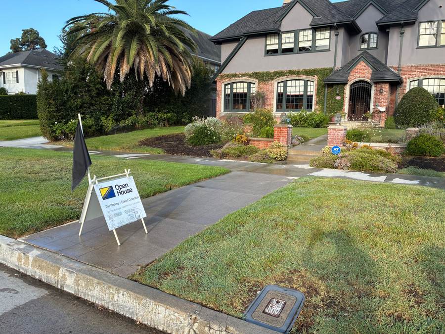 Open house sign and flag placed at a Tudor-style home